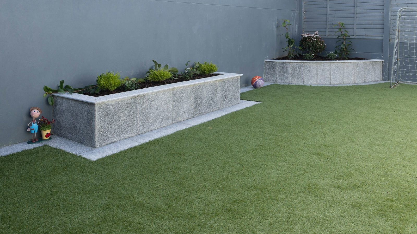 New artificial grass lawn in a walled backyard with two raised planters